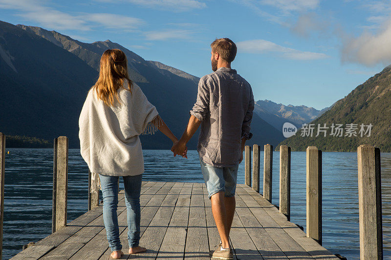 年轻夫妇手牵着手走在湖边的码头上