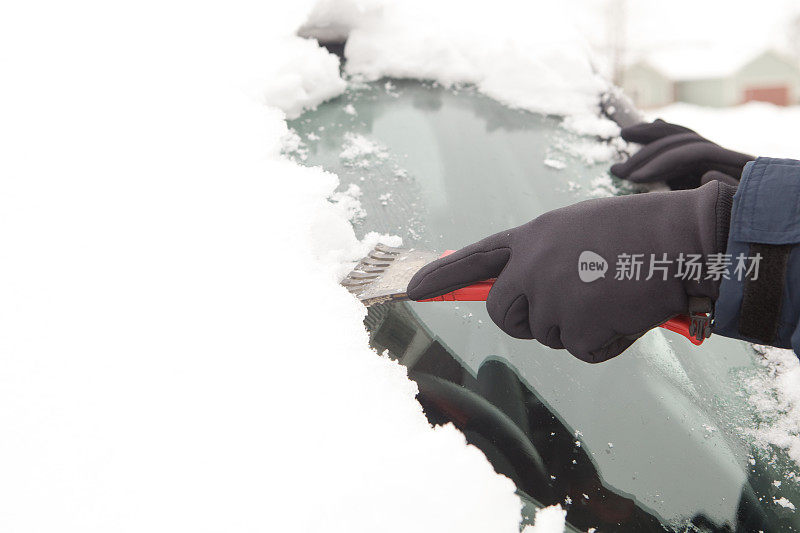 戴着手套的手刮汽车挡风玻璃上的雪和冰。