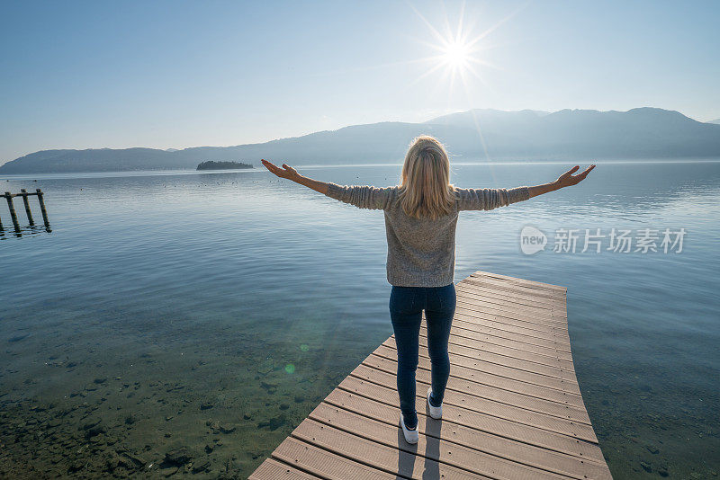 年轻女子在湖边码头上放松，双臂伸展