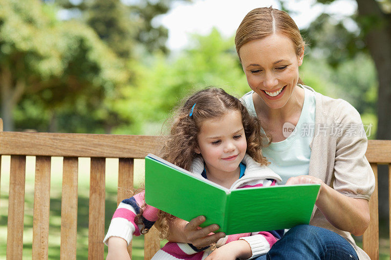 女人笑着和她的女儿一起读书