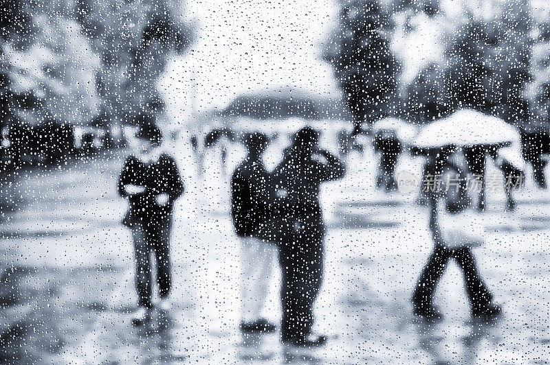 在雨中透过有机玻璃窗户看到撑着雨伞的人们