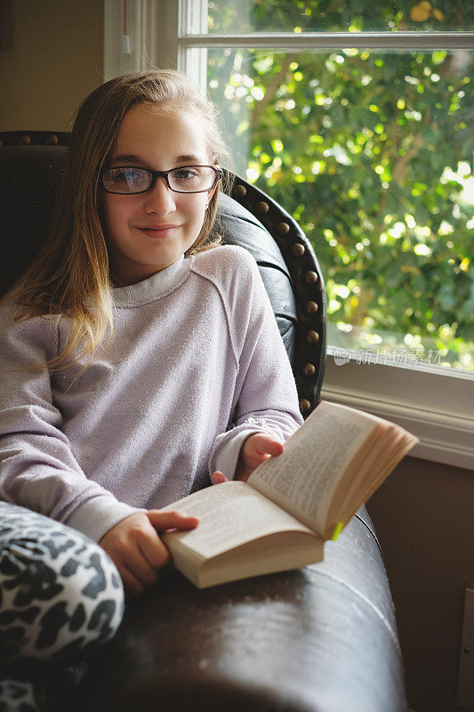 十多岁的女孩在靠近窗户的舒适扶手椅上看书