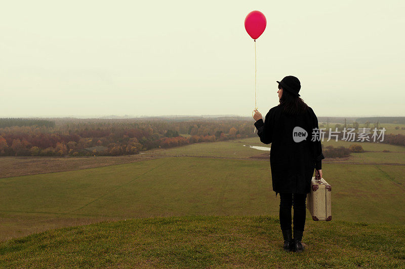 孤独的女人带着手提箱和氦气球旅行