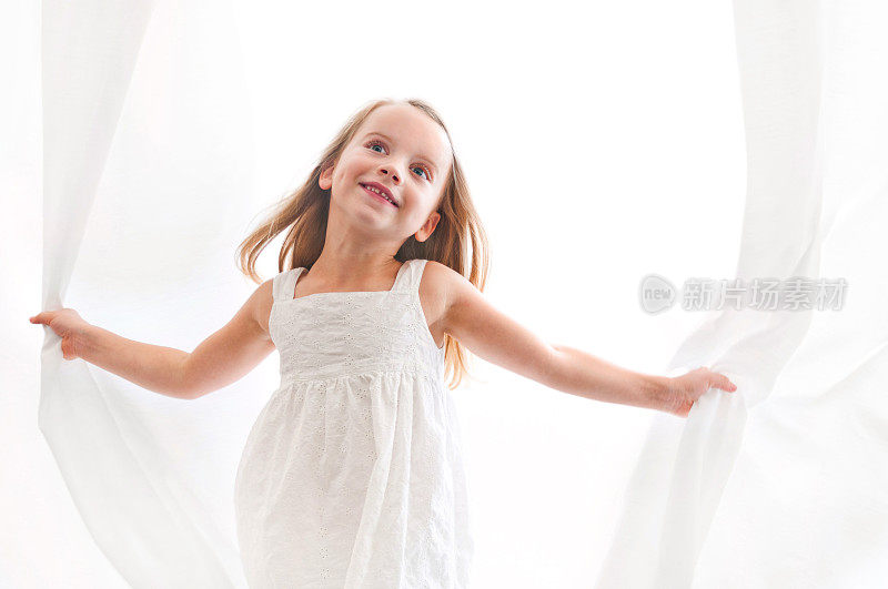 美丽的年轻女孩在白色窗帘中玩耍