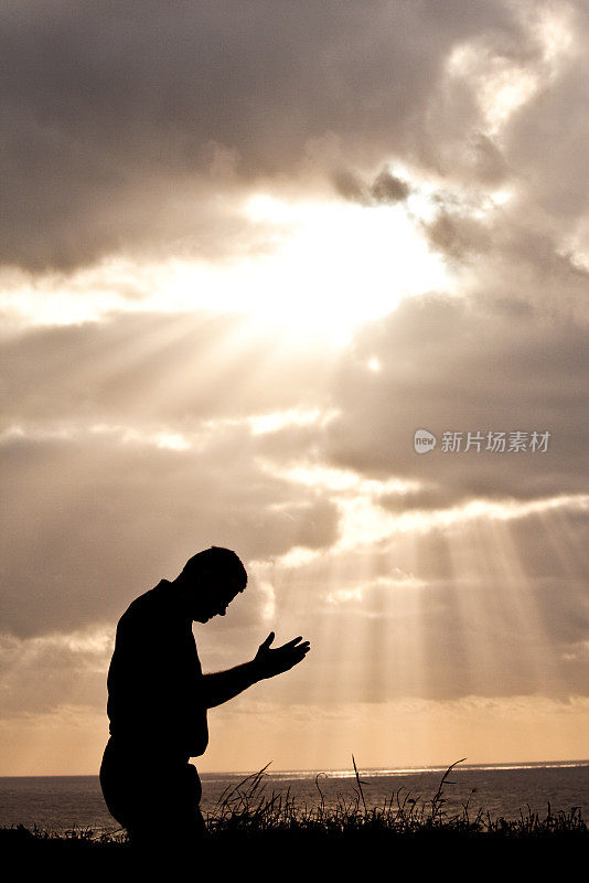 中年男子对着戏剧性的天空祈祷