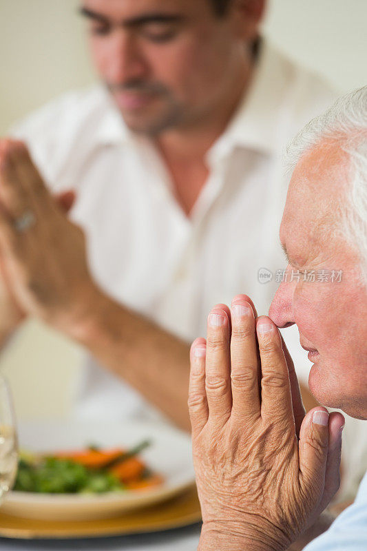 年长的父亲和成年的儿子在饭前祷告