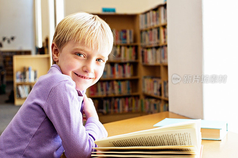 快乐的小女孩在图书馆从书中抬起头，微笑着