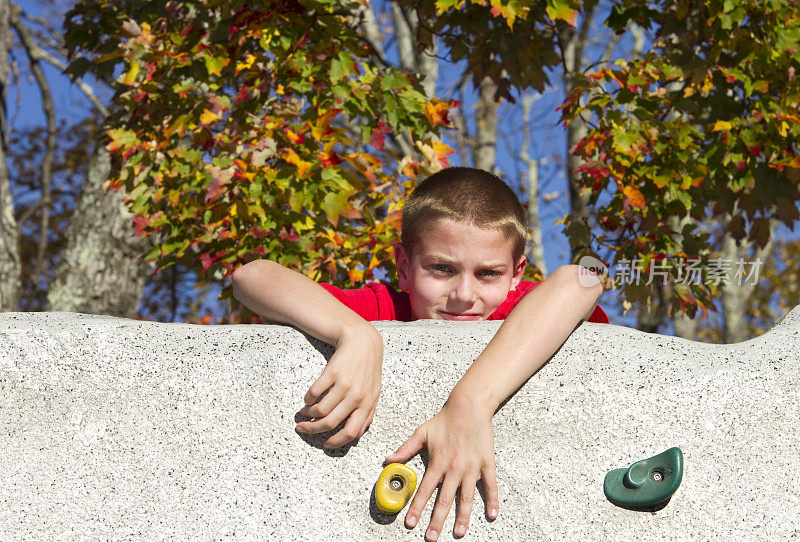 男孩挣扎着爬上石墙，在山顶上窥视