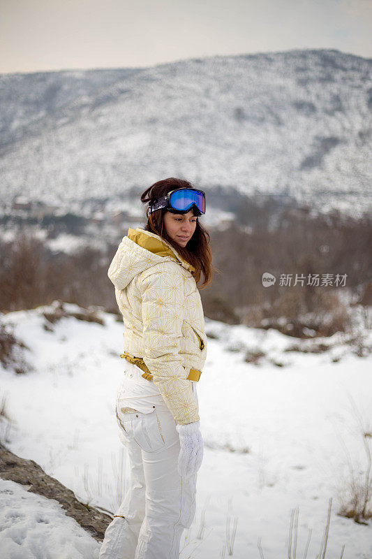 近景美丽的年轻女子在冬天的衣服站在一边，手拿木棍的背景雪山