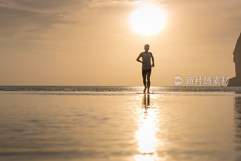 年轻的亚洲男子在海滩上奔跑，夕阳为背景