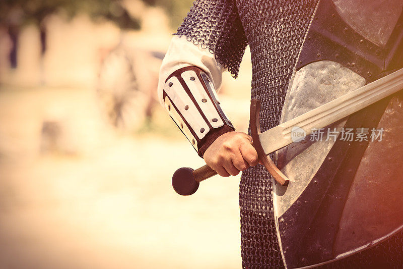 强壮的骑士手与美丽的剑和盾牌上的中世纪装饰背景