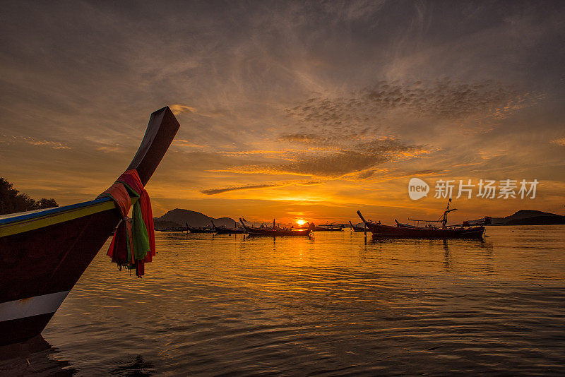 美丽戏剧性的日出在拉威海滩和安达曼长尾船在泰国南部漂浮在普吉岛清澈的海水和阳光照耀