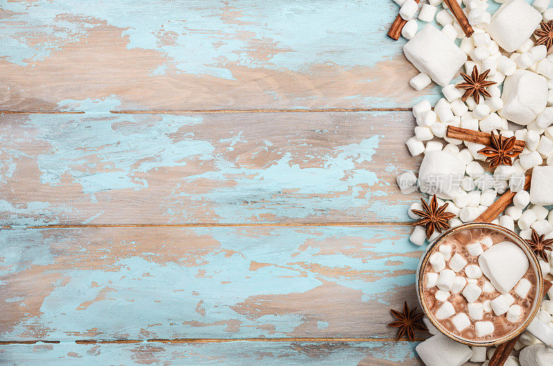 热巧克力，白色棉花糖和冬季香料在蓝色木制背景