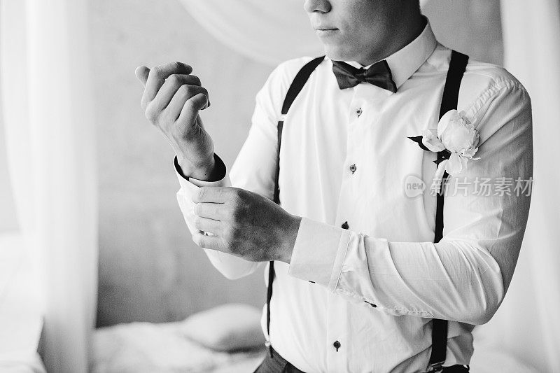 新郎早上准备英俊的新郎在酒店领结吊带打扮和准备婚礼新郎戴袖扣在白衬衫黑白肖像