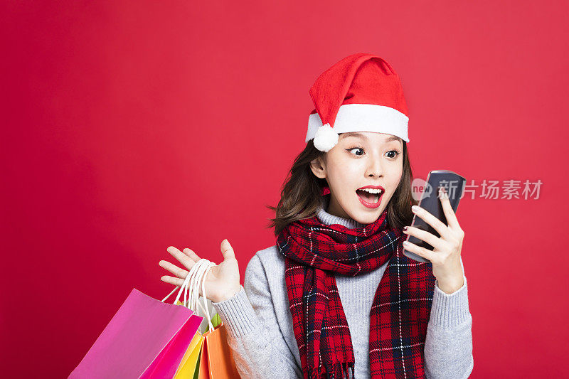 惊讶的女人在买圣诞礼物和看智能手机