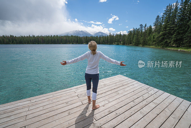 年轻女子在湖边的码头上张开双臂