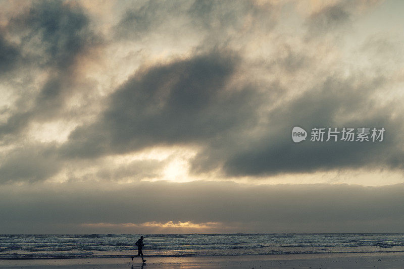 一个人的剪影沿着海滩跑在日落附近。