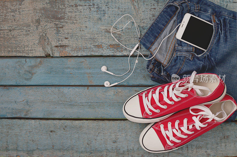 红色复古运动鞋和智能手机与耳机口袋djjinsi在一个蓝色木制背景