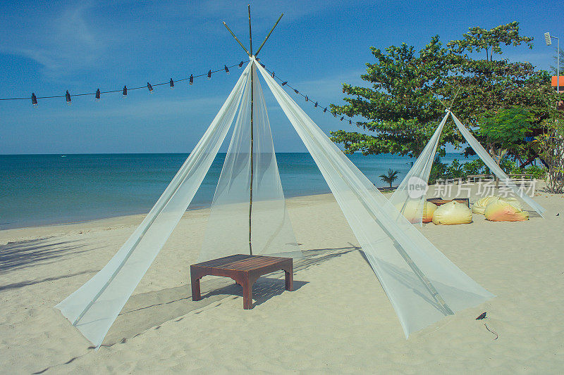 沙滩上白色亭子里的木制甲板椅，美丽的海景和蓝天为背景。