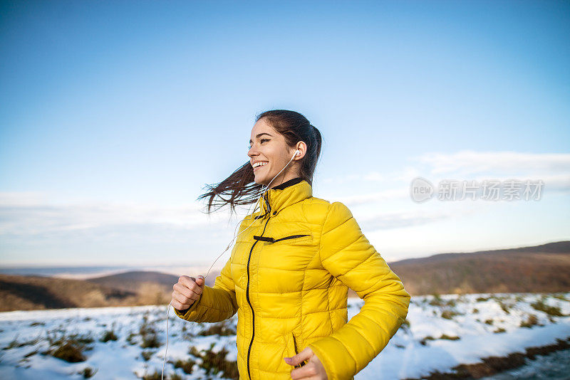 侧面的年轻满意快乐积极和专注的运动活跃的女孩与蓬松的马尾辫在冬季运动服在雪地里跑步。
