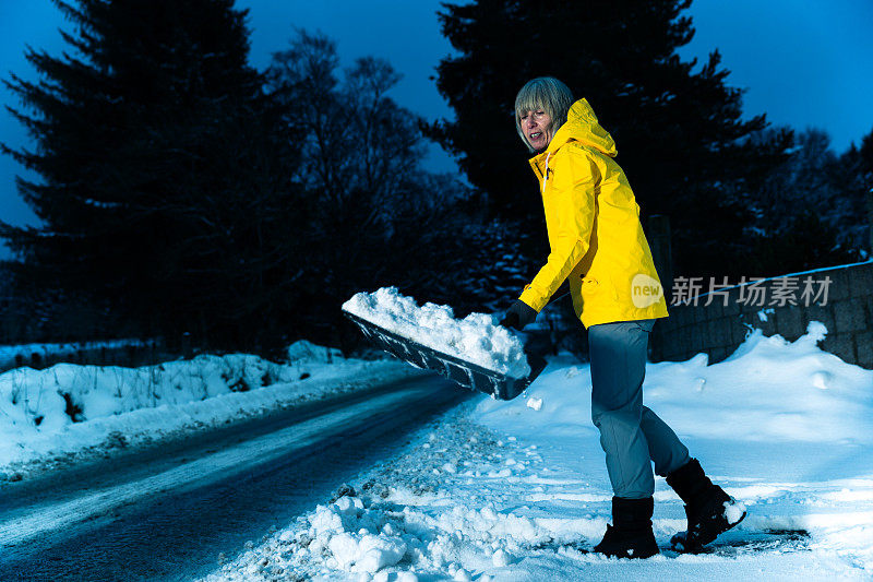 老妇人正在用雪铲清理积雪