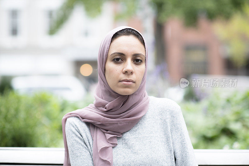 一位年轻的穆斯林妇女带着严肃的表情坐在公园里