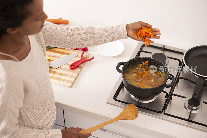 女人把高汤煮开，加入切碎的胡萝卜到汤里。