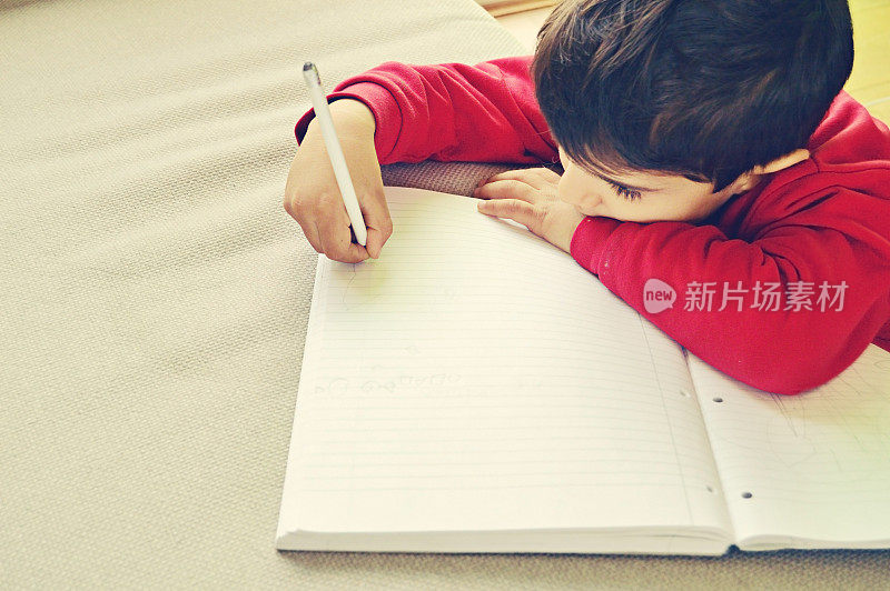 一个穿着红色套头衫的可爱的学龄前儿童正在用铅笔在笔记本上涂鸦