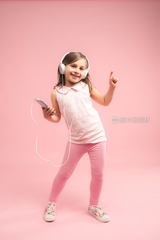 在粉红色背景下听音乐跳舞的小女孩