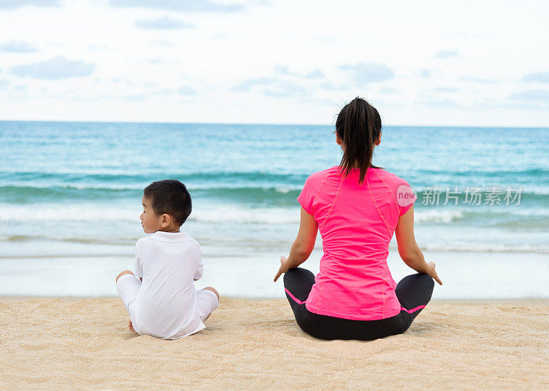 亚洲女人和她的儿子做瑜伽冥想在海滩上