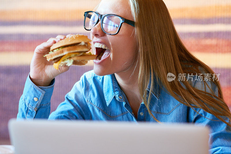 饥饿的自由职业者在咖啡馆里吃汉堡