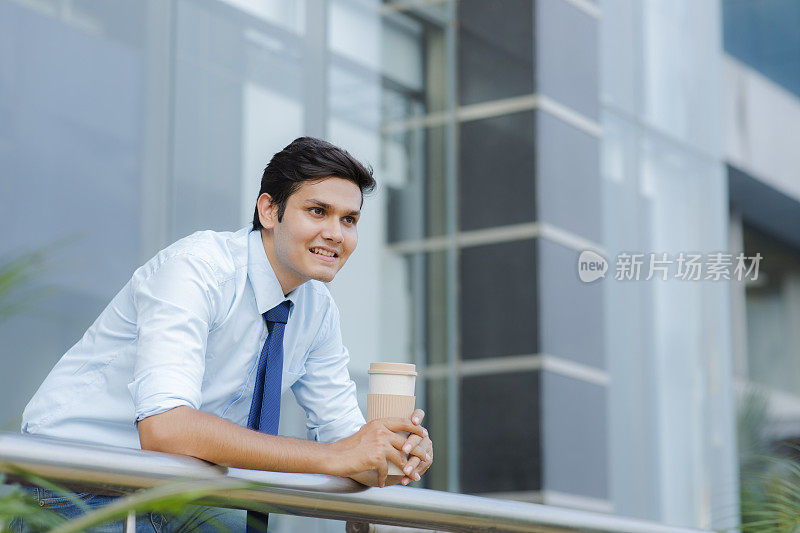 在阳台端着咖啡杯的商人照片