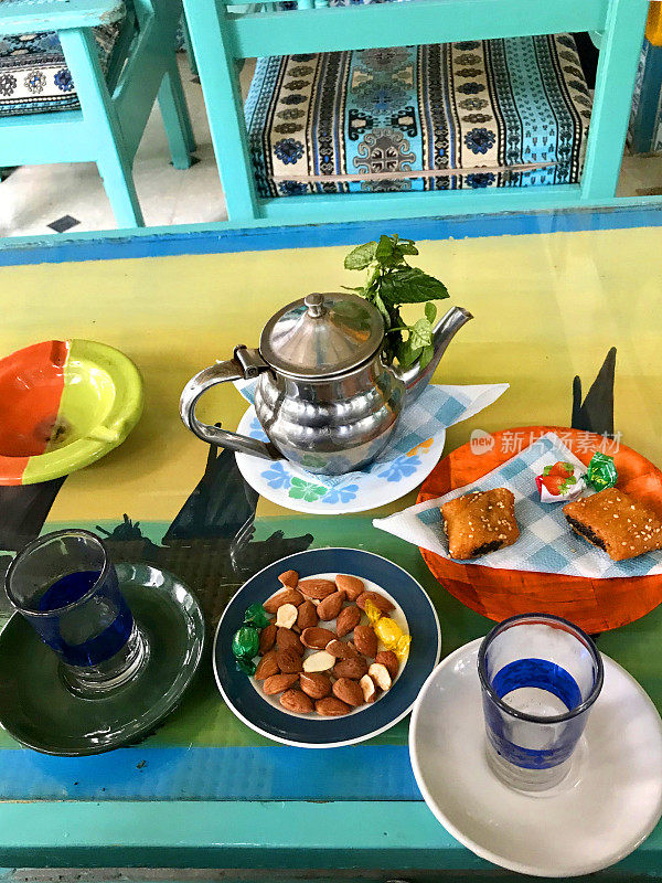 阿拉伯茶杯，茶壶，新鲜薄荷，杏仁和糖果盘子在一个彩色的桌子上