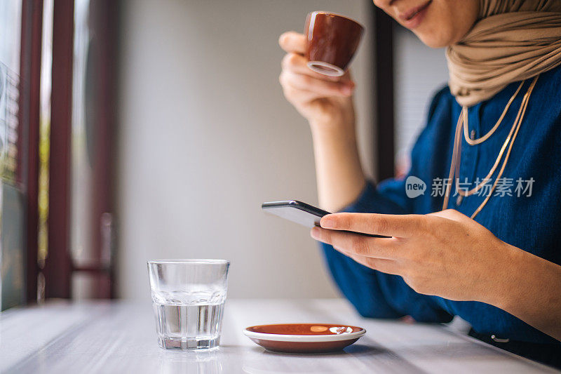 年轻的穆斯林女性在咖啡馆使用智能手机