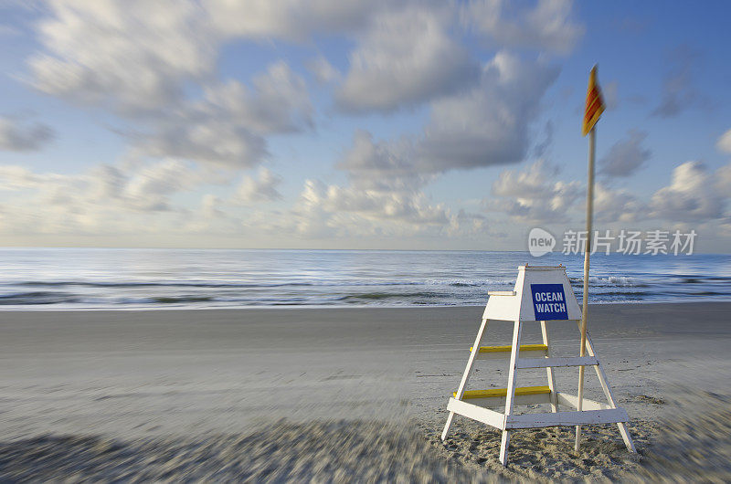 在海滩上:一个救生员站着，手里拿着一面黄色的旗帜，警告人们小心游泳。