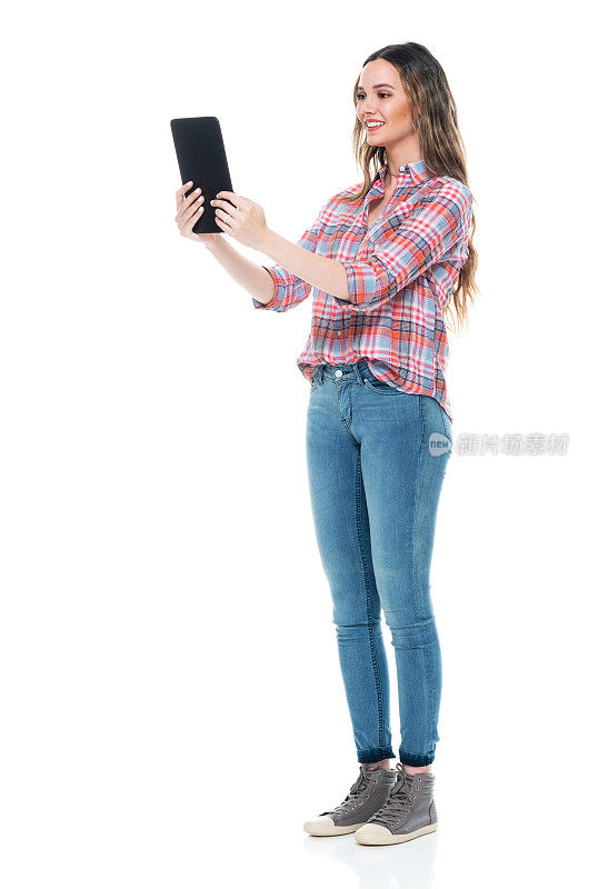 白人女性穿着牛仔裤站在白色背景前使用平板电脑