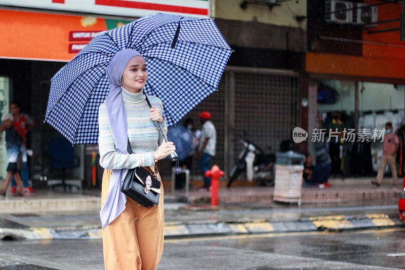 一位戴着头巾、撑着伞的穆斯林马来妇女在雨中行走