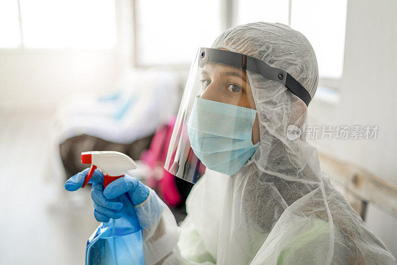 卫生工作者，一名穿着防护服的妇女正在为办公室消毒