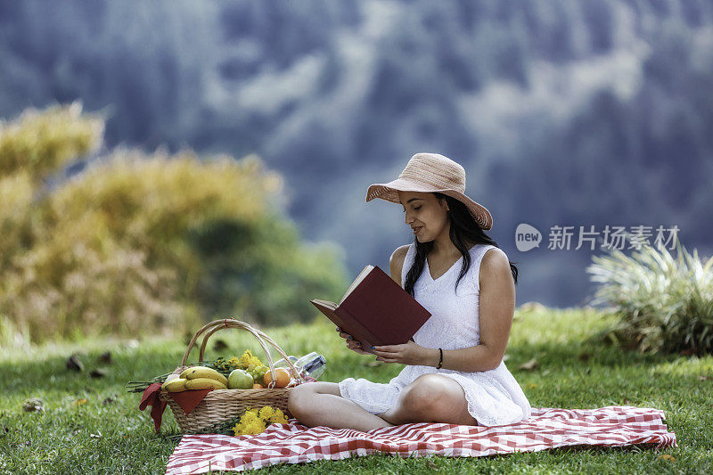 放松可爱的西班牙年轻女子读一本书在草地上。野餐和日间户外休闲活动。