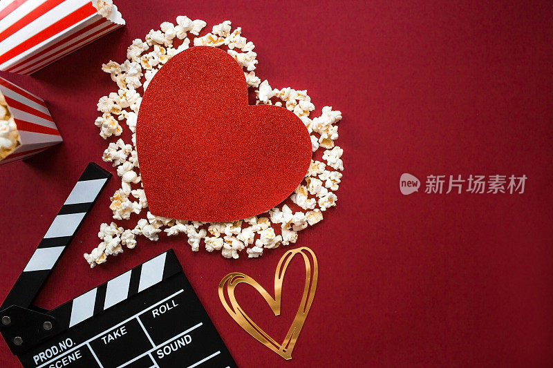 电影工业的一面旗帜。一次浪漫的电影约会。电影摄影机、3D眼镜、爆米花和红色背景上的爆米花心。这部电影将在情人节首映。