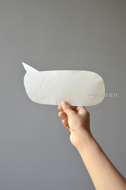 一手拿着空白的白纸，用镂空的剪纸工艺制作出语音泡泡或呼出灰底垂直模板，用于表达思想、交流信息、独白聊天的气球