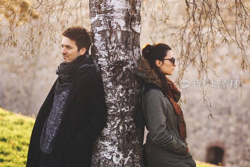 一对年轻夫妇倚在公园的一棵树上