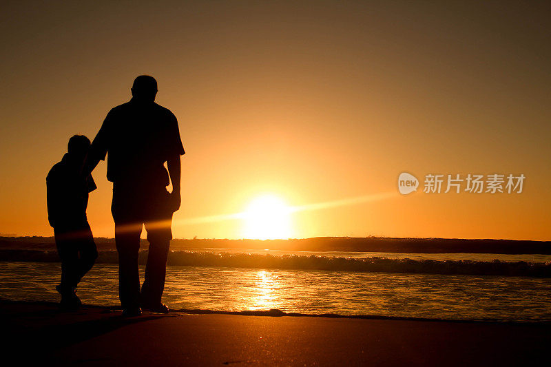 父亲和儿子在沙滩上看日出。
