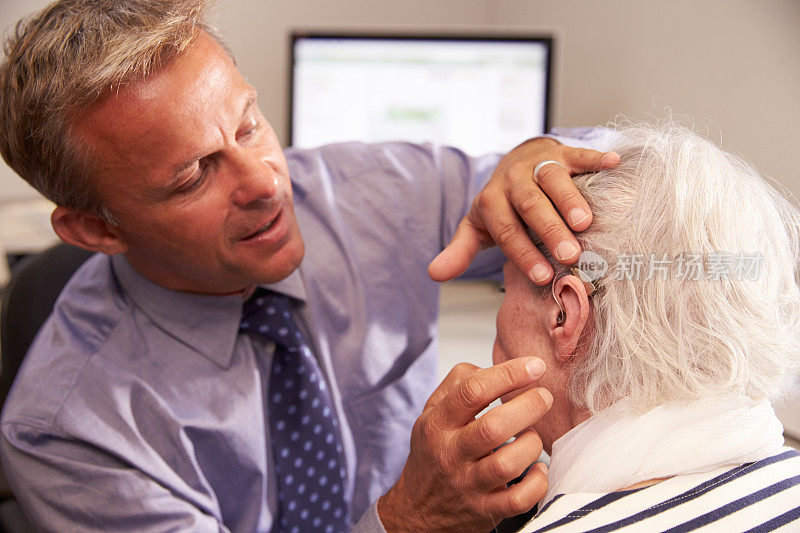 医生为一位年长的女病人安装助听器