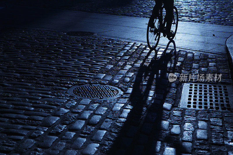 骑自行车的人独自在街角的蓝色夜晚的阴影