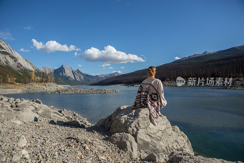 年轻女子坐在湖边的岩石上凝望风景。