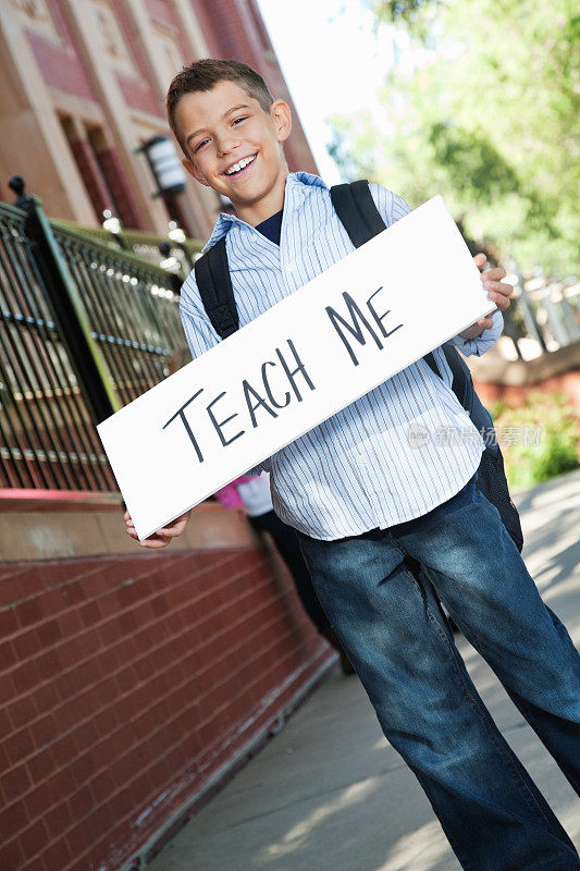 一个快乐的小男孩在教学楼外举着“教我”的牌子