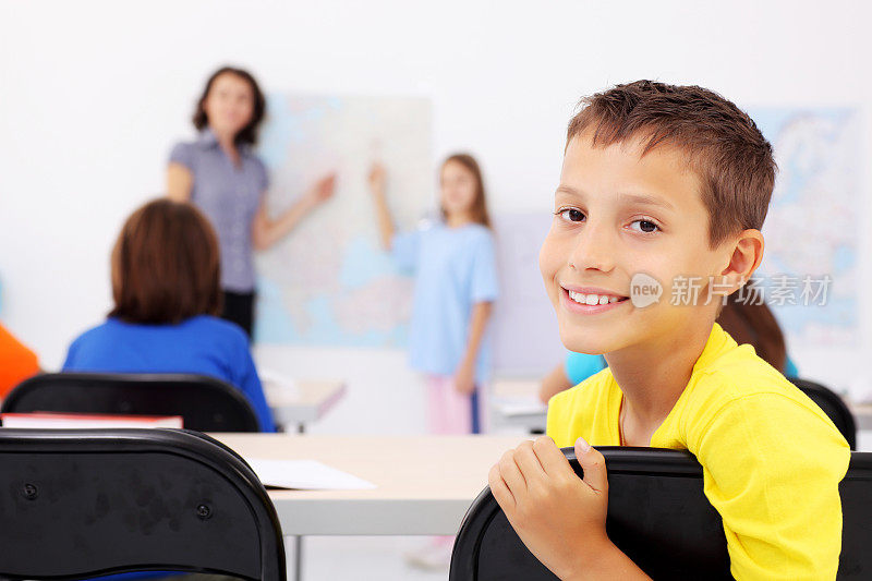 小学生坐在教室里。微笑的男孩转过身来