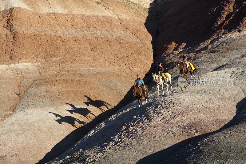 三个骑马的人和一条狗在山坡上投下了影子