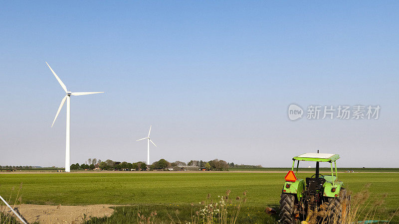 绿色拖拉机在田间，风力涡轮机在背景